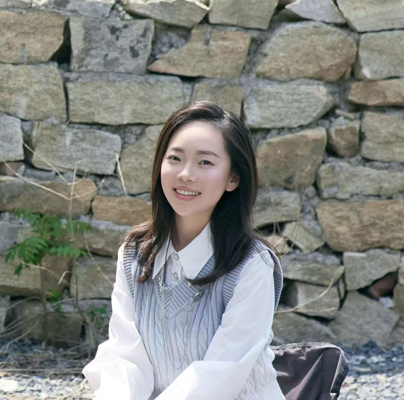 Meijun Gao smiling outdoors in front of a stone wall